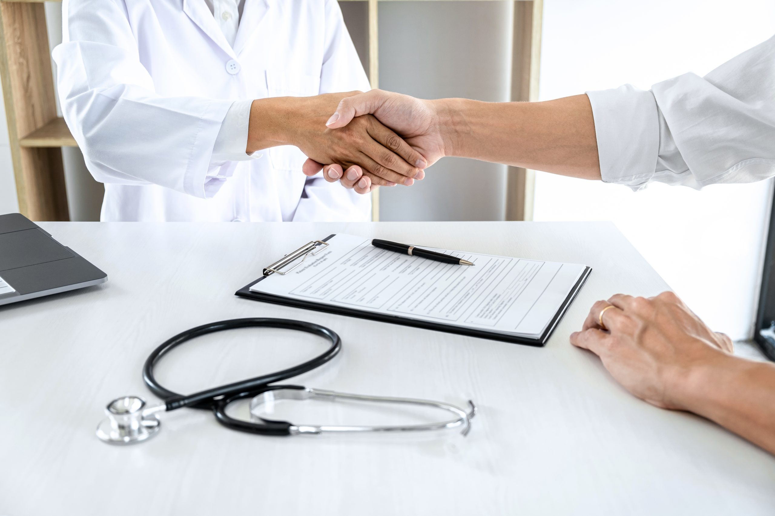 doctor and patient shaking hands over desk with stethoscope and notepad